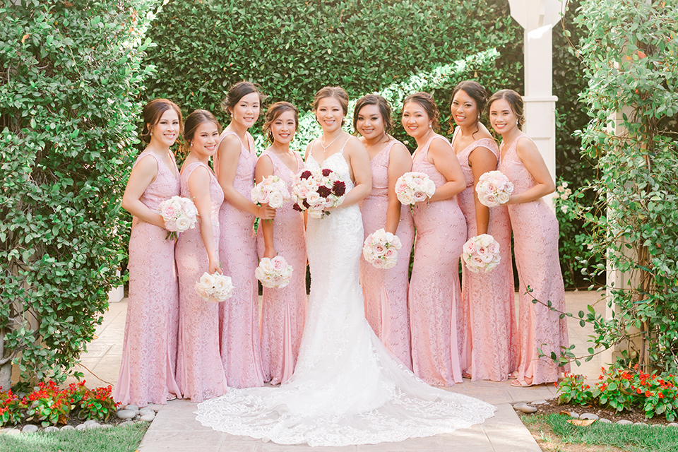  bride in a lace formfitting gown and a high neckline and the bridesmaids in a rose blush gowns