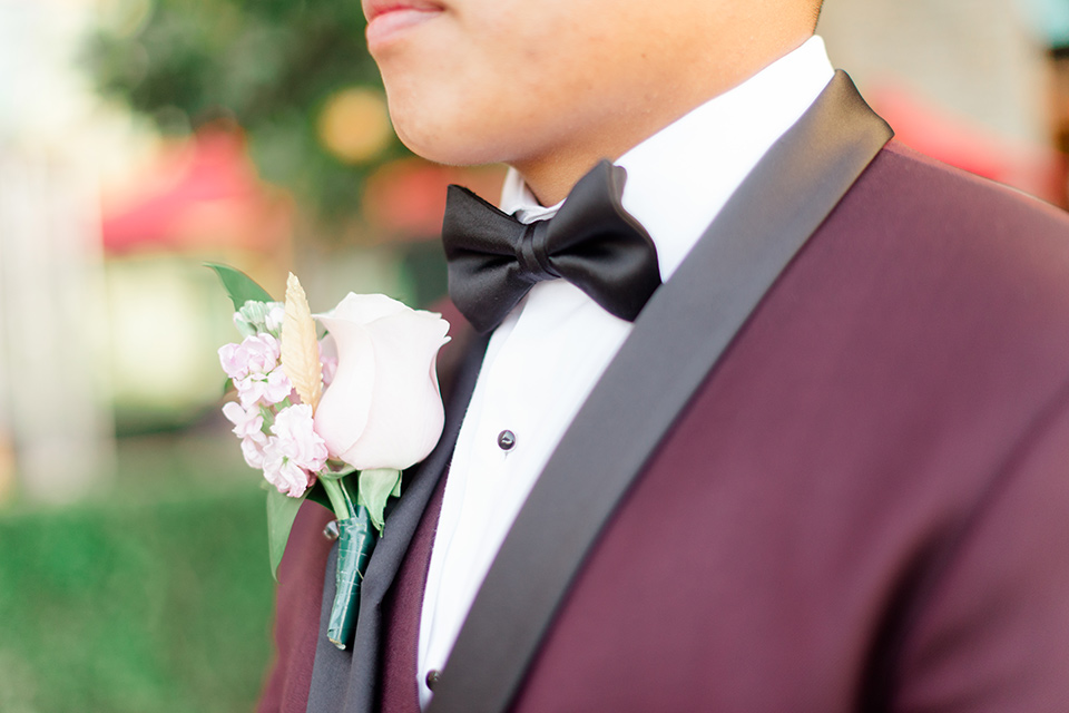  groom in a burgundy tuxedo with a black bow tie