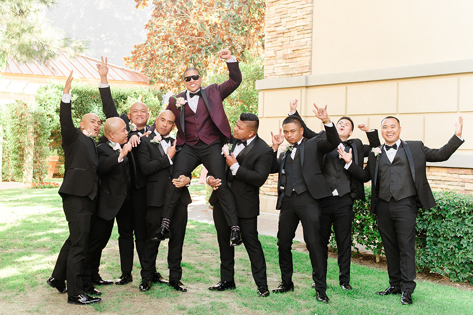  groom in a burgundy tuxedo with a black bow tie and the groomsmen in a black tuxedo with a black bow tie 