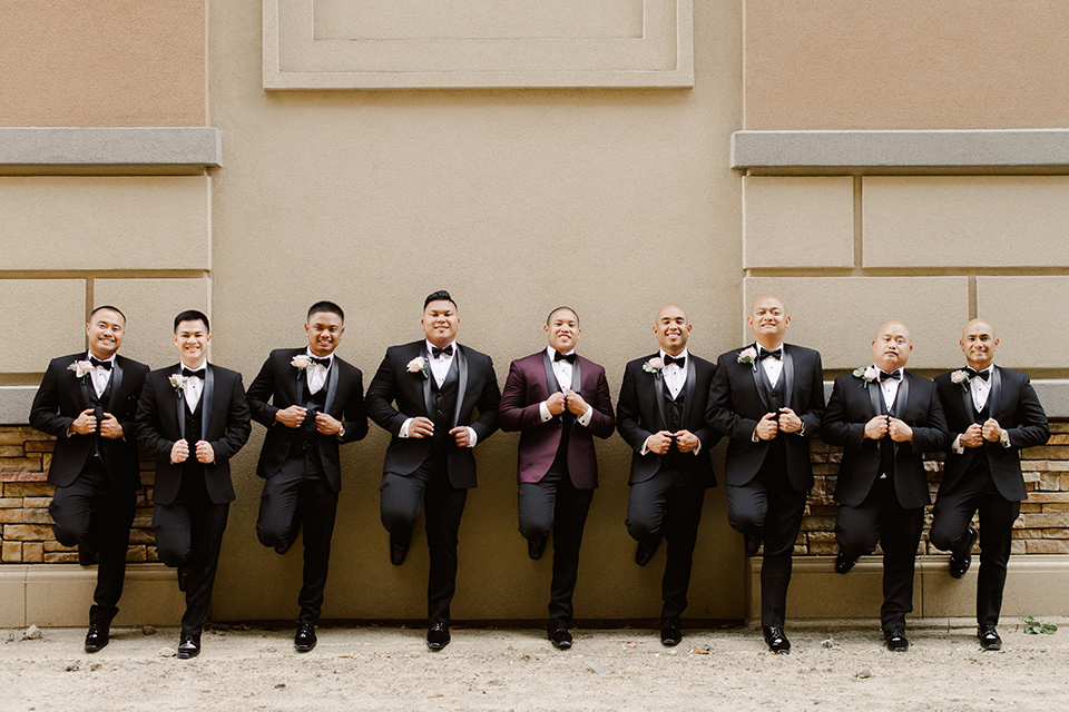  groom in a burgundy tuxedo with a black bow tie and the groomsmen in a black tuxedo with a black bow tie 