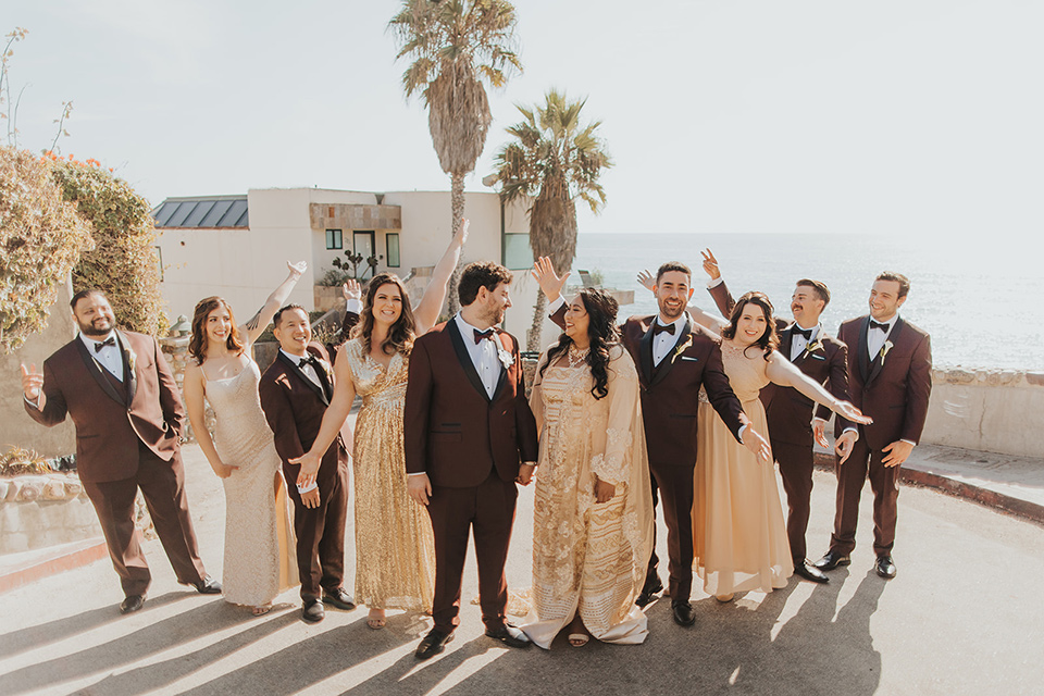  bride in a cultural Burmese gown, the groom in a burgundy tuxedo with a black shawl, the bridesmaids in gold gowns, and the groomsmen in black tuxedos 