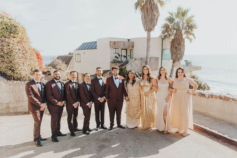  bride in a cultural Burmese gown, the groom in a burgundy tuxedo with a black shawl, the bridesmaids in gold gowns, and the groomsmen in black tuxedos 