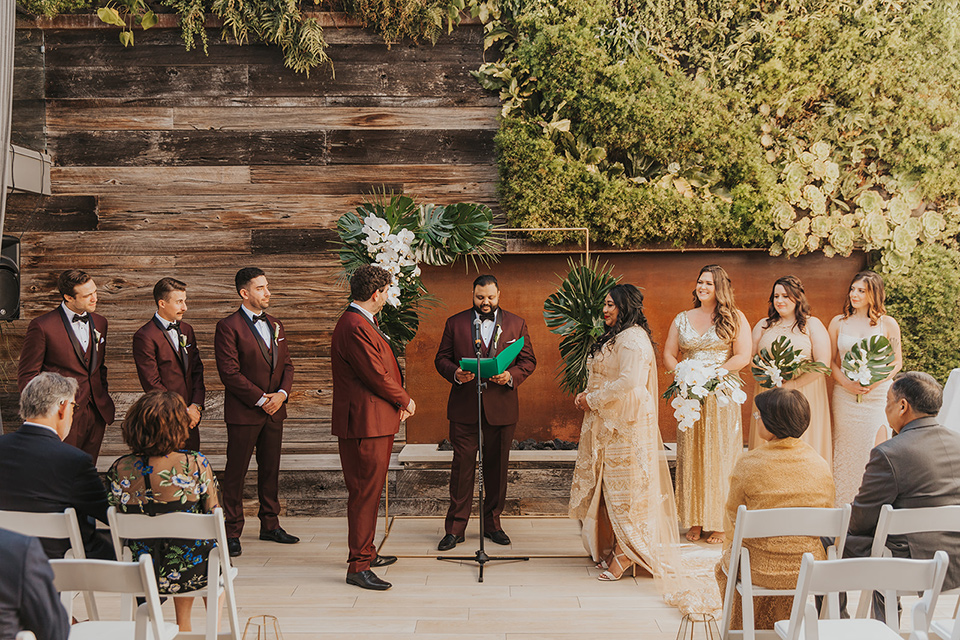  bride in a cultural Burmese gown, the groom in a burgundy tuxedo with a black shawl, the bridesmaids in gold gowns, and the groomsmen in black tuxedos 