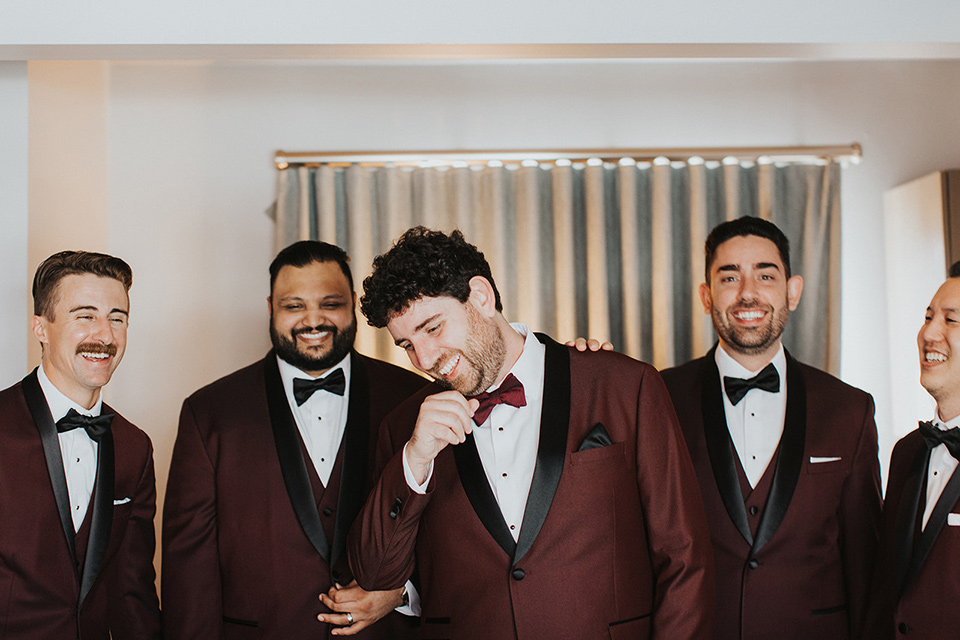  the groom in a burgundy tuxedo with a black shawl and the groomsmen in black tuxedos 