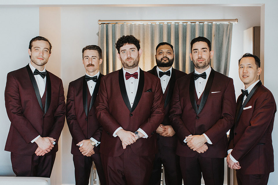  the groom in a burgundy tuxedo with a black shawl and the groomsmen in black tuxedos 