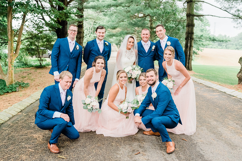 bride in a white modern lace gown with a cathedral veil and the groom in a cobalt blue suit, the bridesmaids in blush pink gown and the groomsmen in cobalt blue suits