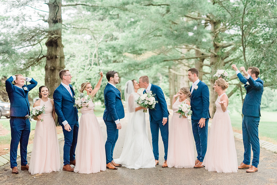  bride in a white modern lace gown with a cathedral veil and the groom in a cobalt blue suit, the bridesmaids in blush pink gown and the groomsmen in cobalt blue suits