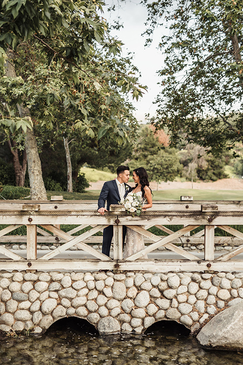  bride in a white lace gown with a crystal bodice and a deep v neckline and the groom in a navy notch lapel suit with a white long tie and brown shoes