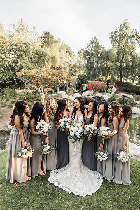  bride in a white formfitting gown and the groom in a navy suit with brown shoes and white long tie, the bridesmaids in light dusty sage gowns and groomsmen in navy blue suits and blue ties 