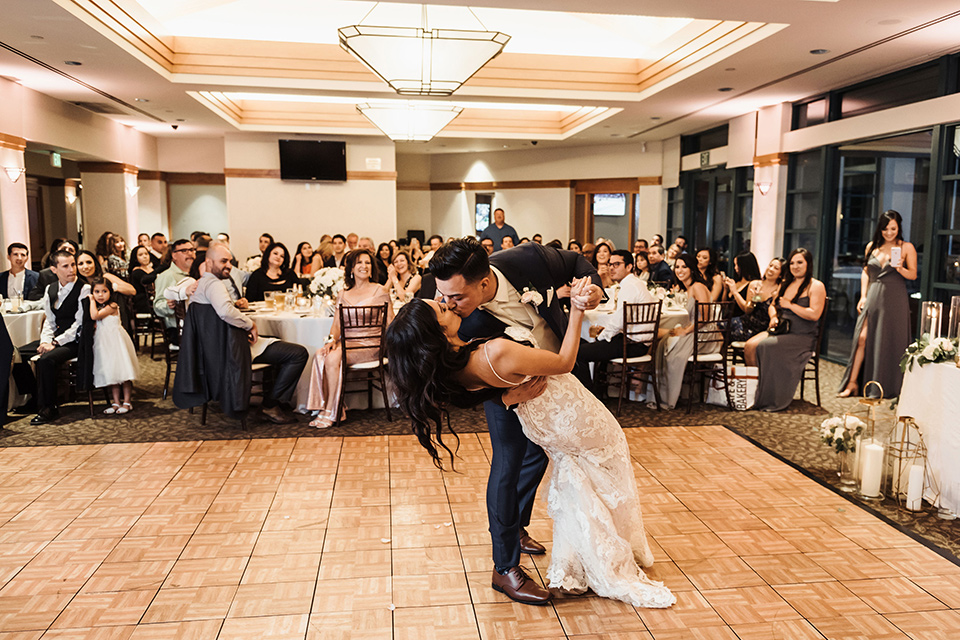  bride in a white formfitting gown and the groom in a navy suit with brown shoes and white long tie during first dance