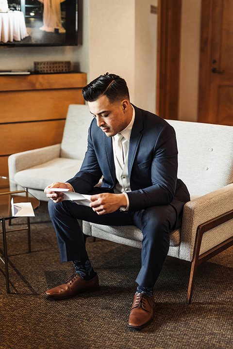  the groom in a navy notch lapel suit with a white long tie and brown shoes first kiss 