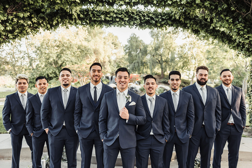  the groom in a navy suit with brown shoes and white long tie and groomsmen in navy blue suits and blue ties 