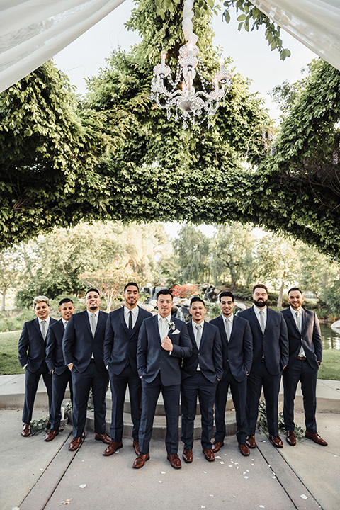  bride in a white lace gown with a crystal bodice and a deep v neckline and the groom in a navy notch lapel suit with a white long tie and brown shoes first kiss 