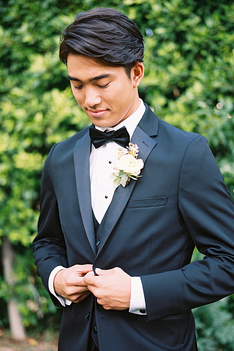  the groom in a sleek black notch lapel tuxedo with a simple black bow tie