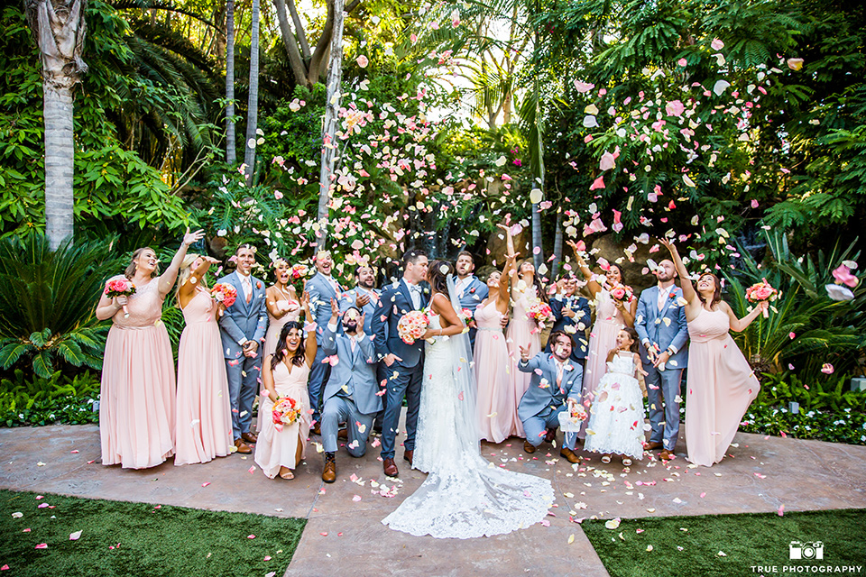  bride in a formfitting lace gown and the groom in a charcoal tuxedo, the bridesmaids in pink gowns, and groomsmen in light blue suits