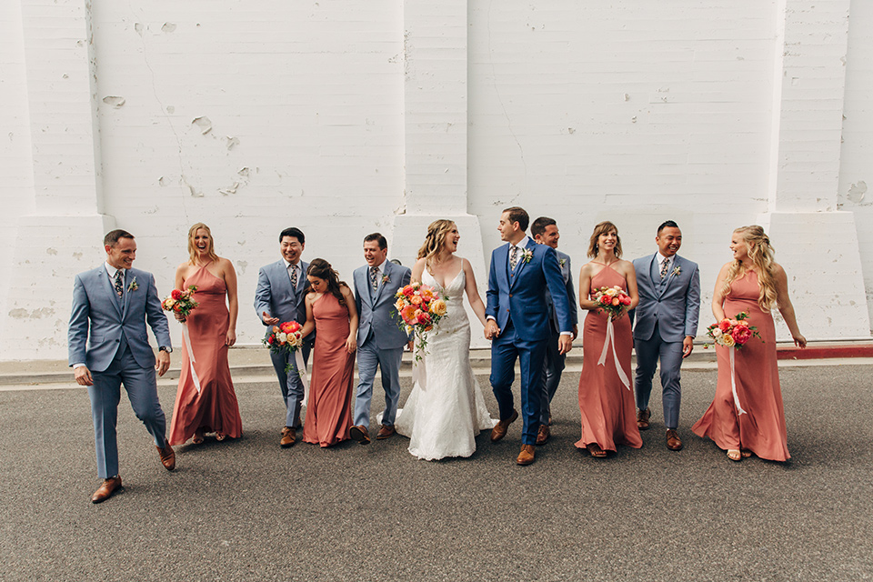  bride in a formfitting lace gown and the groom in a blue suit, the bridesmaids in desert sunset colored gowns, and the groomsmen in light blue suits