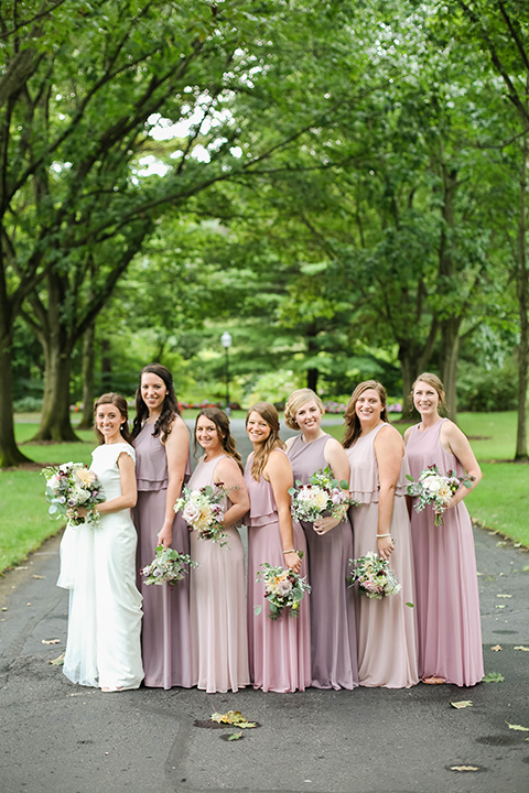  bride in a white gown with a high neckline and veil and bridesmaids in mauve and pink dresses 