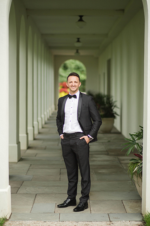  groom in a black tuxedo with a black bow tie and accessories 