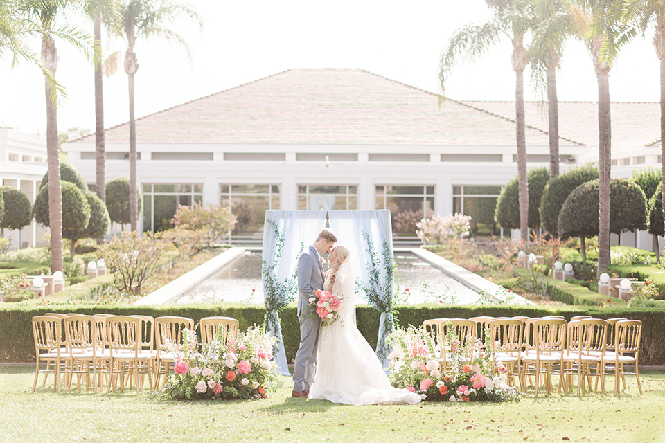 bride in a white ballgown with a French braid style hairstyle and the groom in a light blue suit with a white long tie at ceremony