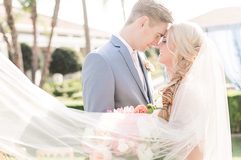 bride in a white ballgown with a French braid style hairstyle and the groom in a light blue suit with a white long tie under veil