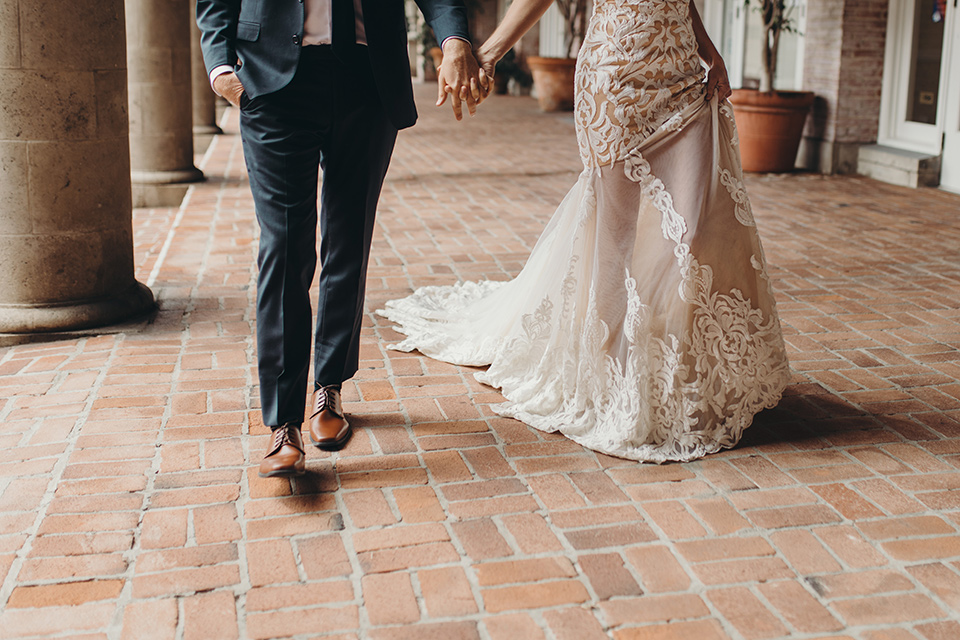  bride in a white lace gown with an illusion neckline and flowing train and the groom in a navy notch lapel suit with a deep teal long tie 