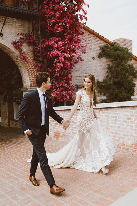  bride in a white lace gown with an illusion neckline and flowing train and the groom in a navy notch lapel suit with a deep teal long tie 