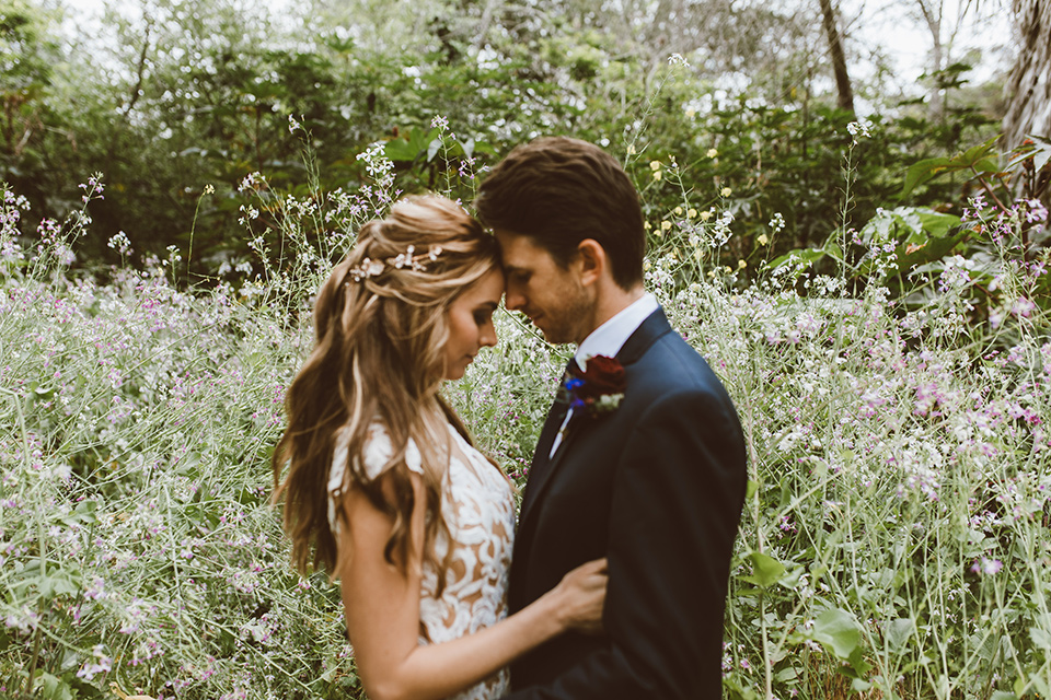  bride in a white lace gown with an illusion neckline and flowing train and the groom in a navy notch lapel suit with a deep teal long tie 