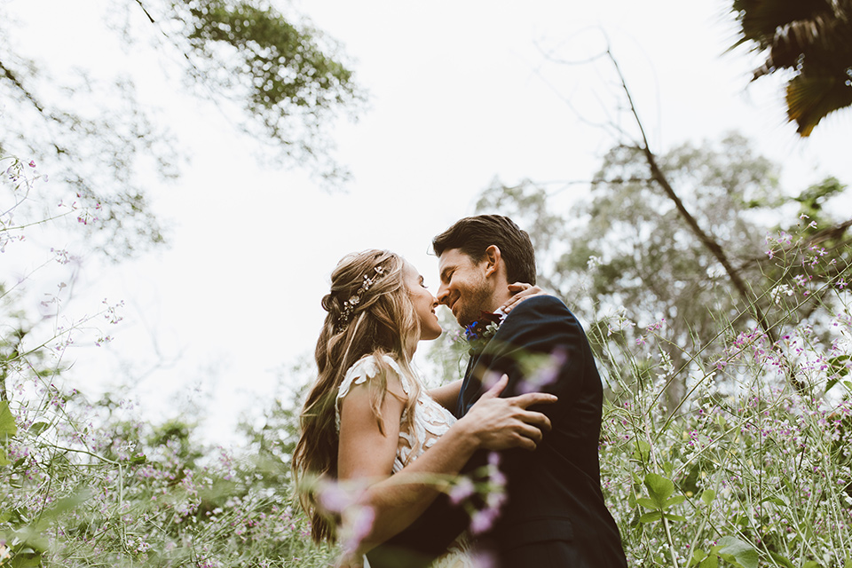  bride in a white lace gown with an illusion neckline and flowing train and the groom in a navy notch lapel suit with a deep teal long tie 