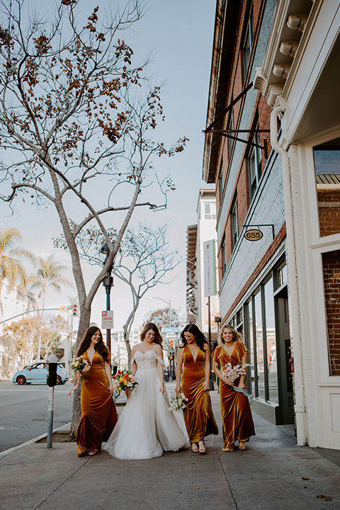  bride in a full skirt gown with an off the shoulder detail and the bridesmaids in burnt orange velvet gowns 