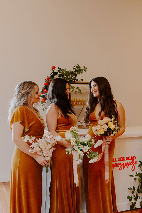  bride in a full skirt gown with an off the shoulder detail and the bridesmaids in burnt orange velvet gowns