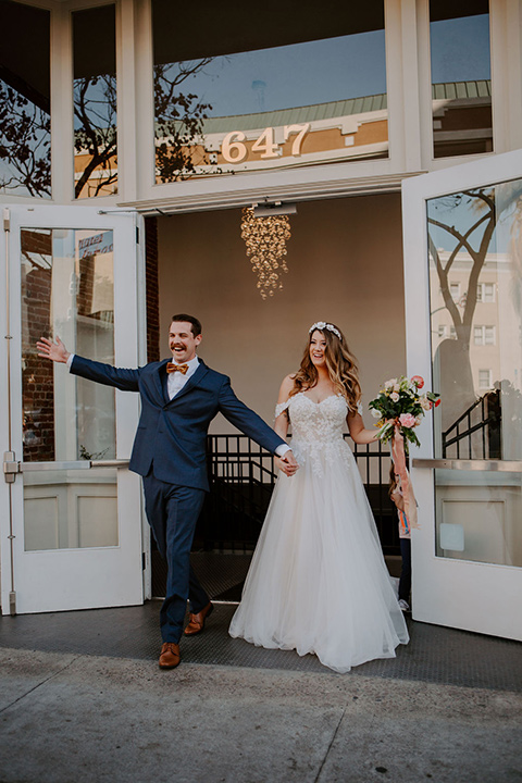  bride in a full skirt gown with an off the shoulder detail and the groom in dark blue suit and bow tie