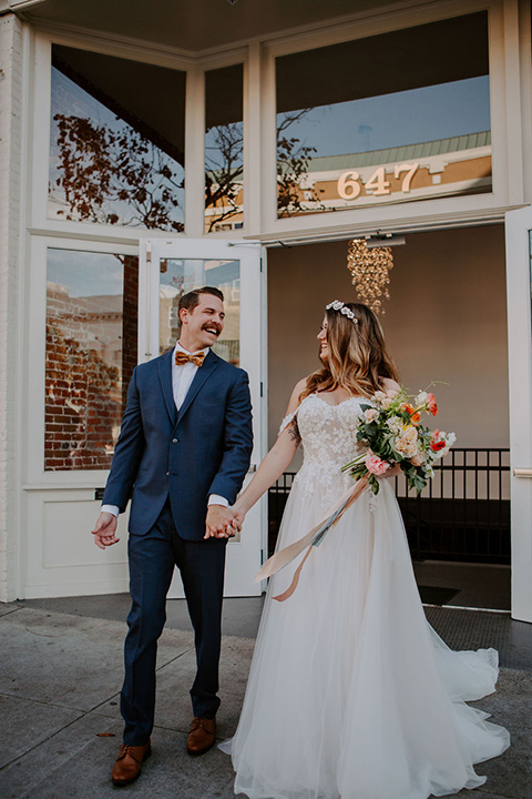  bride in a full skirt gown with an off the shoulder detail and the groom in dark blue suit and bow tie 