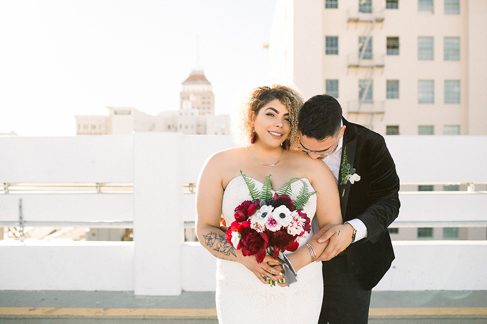  the bride is in a white formfitting lace gown with a sweetheart neckline and fun velvet shoes and the groom in a black velvet tuxedo with a cropped pant and bow tie on the roof