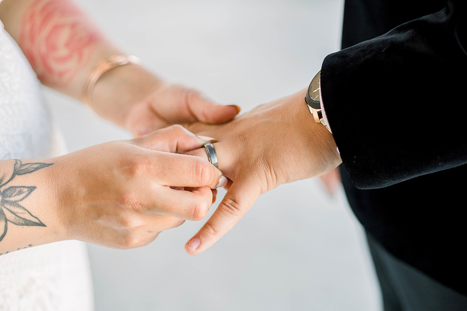  the bride is in a white formfitting lace gown with a sweetheart neckline and fun velvet shoes and the groom in a black velvet tuxedo with a cropped pant and bow tie exchanging rings