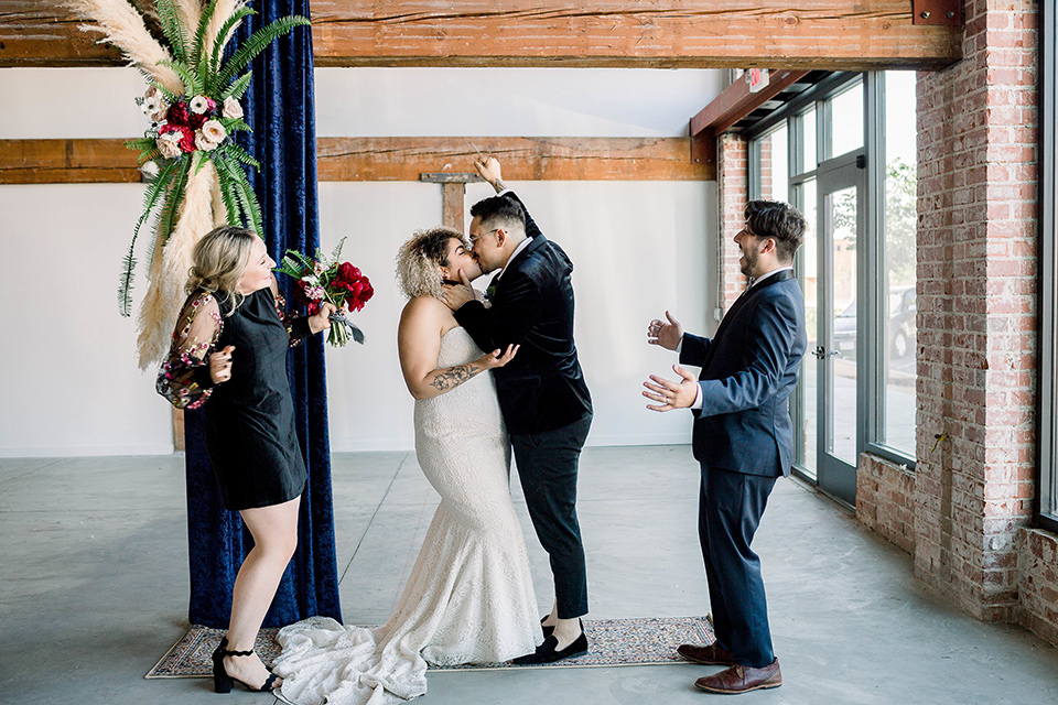  the bride is in a white formfitting lace gown with a sweetheart neckline and fun velvet shoes and the groom in a black velvet tuxedo with a cropped pant and bow tie exchanging rings