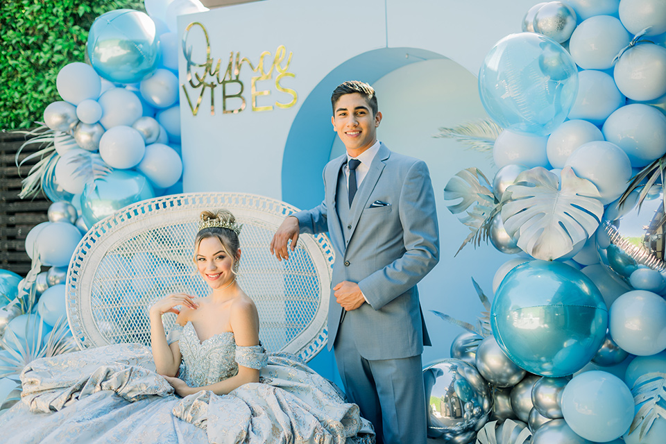  chambelan in a light blue suit and navy long tie and blue pocket square and the birthday girl in a bohemian chair 