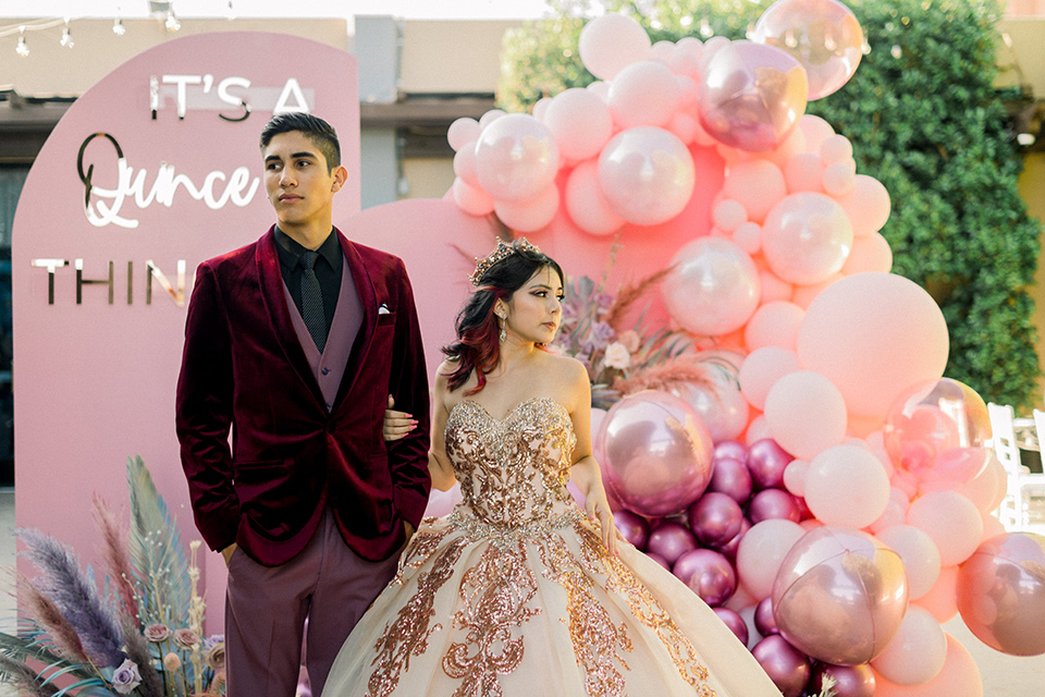  chambelanes style with a burgundy velvet tuxedo, rose pink pants and vest, and a black shirt and the birthday girl in a gold and pink gown with a strapless neckline and lace detailing 