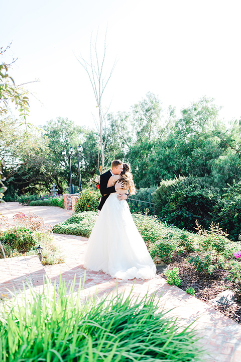  groom in a black tuxedo with a black bow tie and the bride in a white lace fit and flare gown embracing 