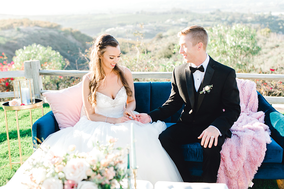  groom in a black tuxedo with a black bow tie and the bride in a white lace fit and flare gown sitting on a couch at the reception