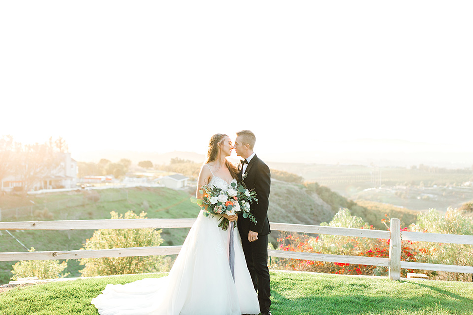  groom in a black tuxedo with a black bow tie and the bride in a white lace fit and flare gown looking at the camera