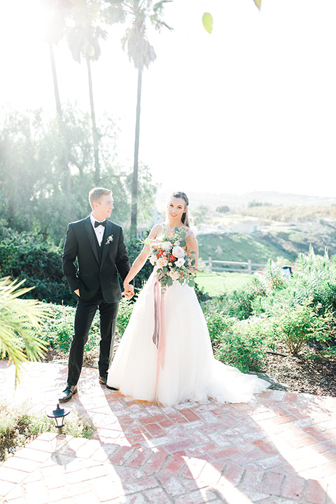  groom in a black tuxedo with a black bow tie and the bride in a white lace fit and flare gown embracing 