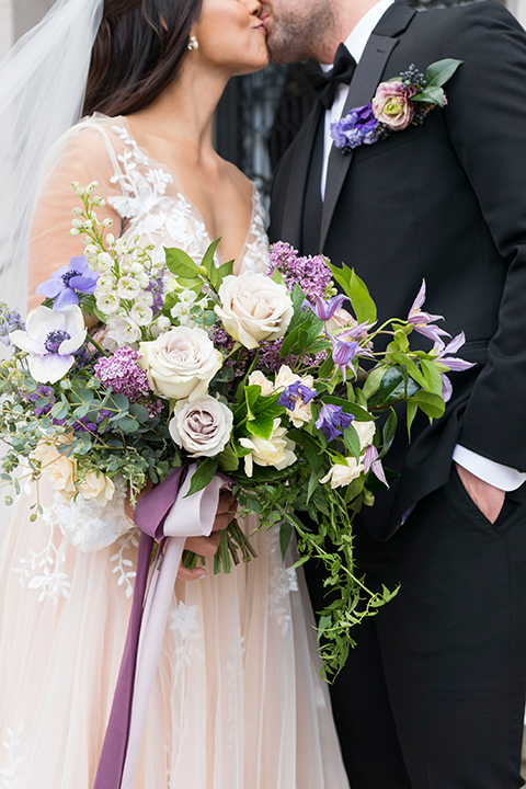  bride in a white lace ballgown with a sweetheart neckline and a regal looking crown and the groom in a black tuxedo with a black bow tie and pocket square close up 