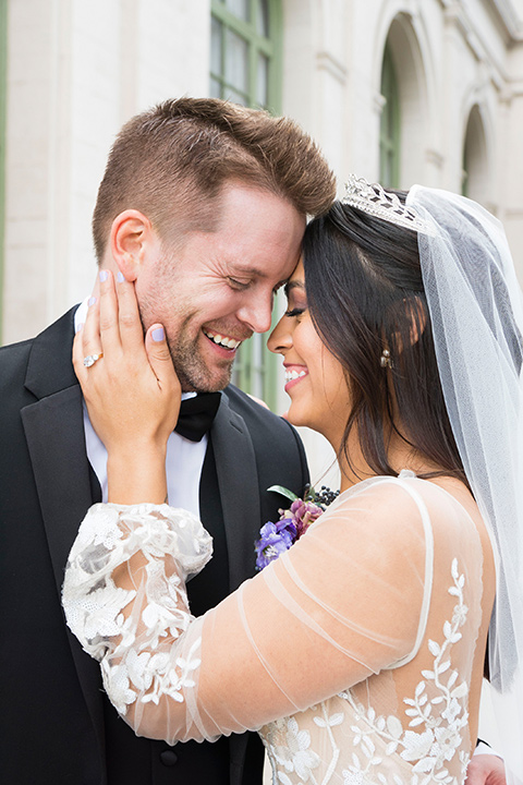  bride in a white lace ballgown with a sweetheart neckline and a regal looking crown and the groom in a black tuxedo with a black bow tie and pocket square close up 