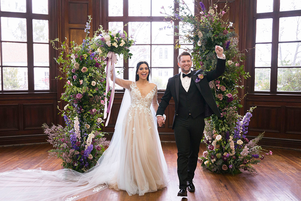  bride in a white lace ballgown with a sweetheart neckline and a regal looking crown and the groom in a black tuxedo with a black bow tie and pocket square ceremony at historic venue