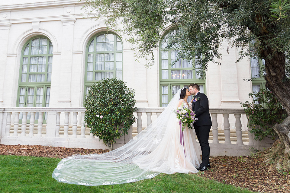  bride in a white lace ballgown with a sweetheart neckline and a regal looking crown and the groom in a black tuxedo with a black bow tie and pocket square ceremony at historic venue