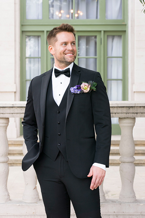  groom in a black tuxedo with a black bow tie and purple pocket square