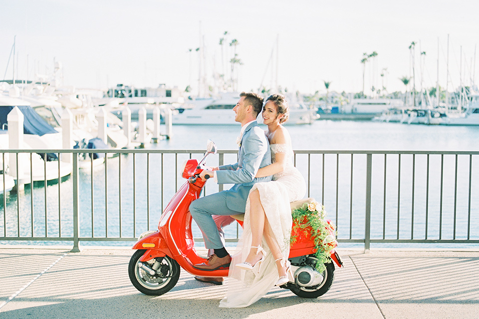  bride in a form fitting gown with an off the shoulder detail and the groom in a light blue suit on the vespa 