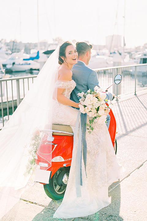  bride in a form fitting gown with an off the shoulder detail and the groom in a light blue suit with the vespa