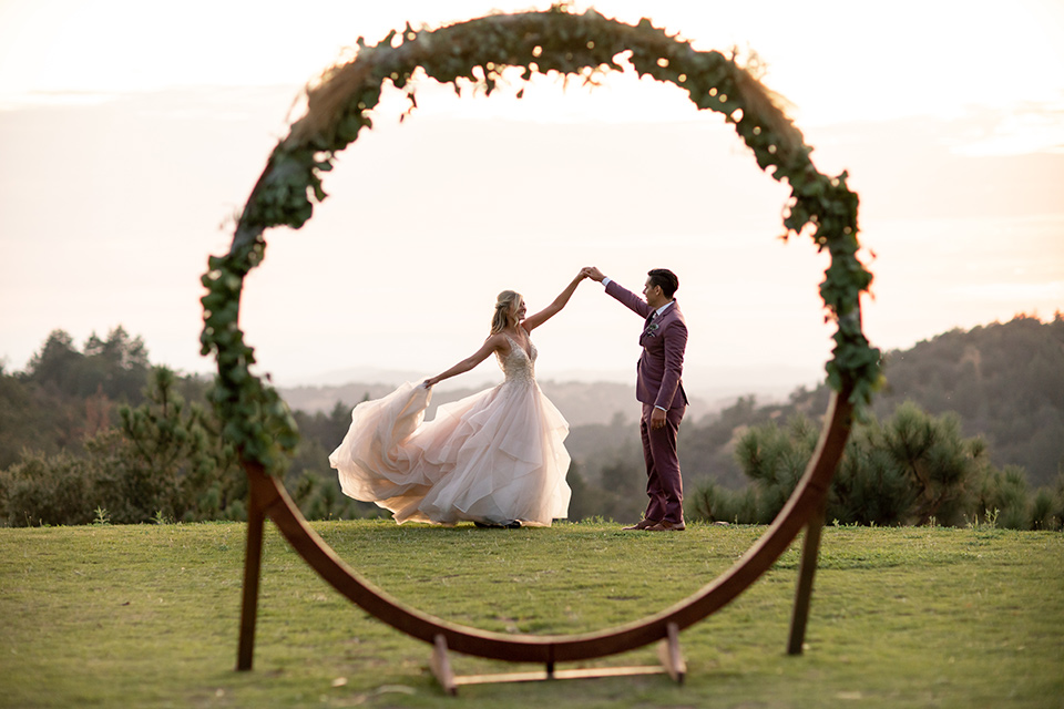  bride in a white ballgown with a deep-v neckline and crystal embellishments and the groom in a rose pink suit with a navy floral neck tie 