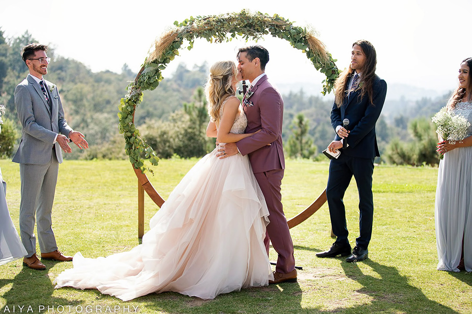  bride in a white ballgown with a deep-v neckline and crystal embellishments and the groom in a rose pink suit with a navy floral neck tie 